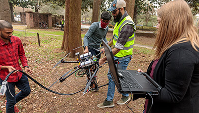 Students working with water collecting drone next to small body of water.