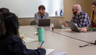 Students and faculty sitting at a table discussing. 